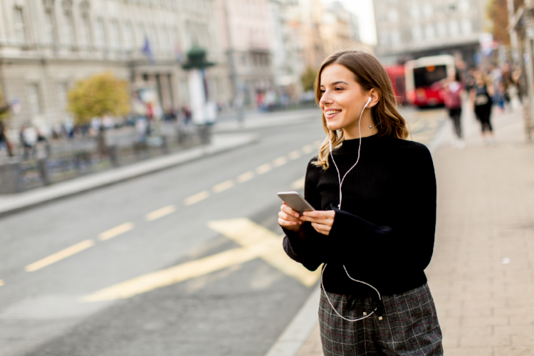 Young brunette woman using mobile while standing on street and  waiting for a bus or taxi
